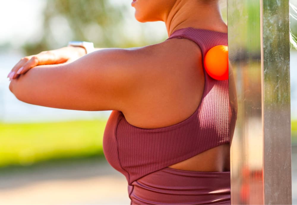 woman holding massage ball between shoulder blades