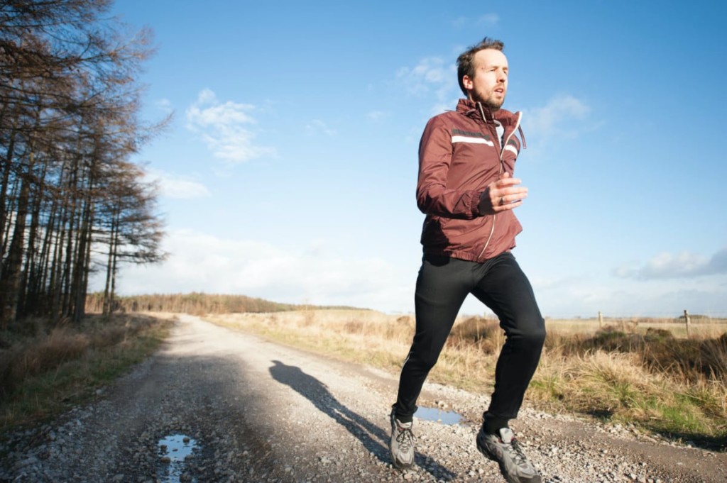 man running nearby a forest and a field